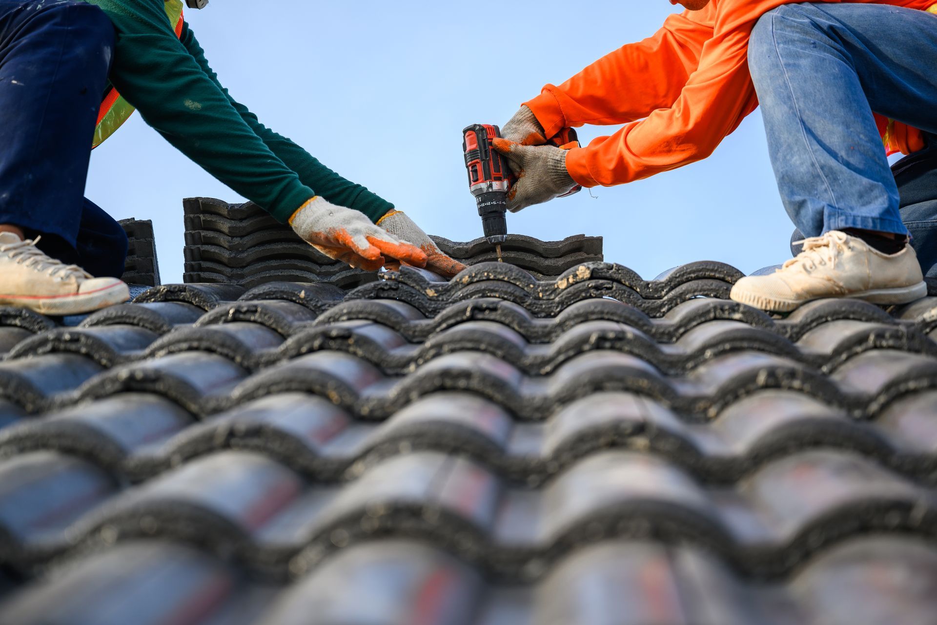 Two workers installing roof tiles, one using a drill.