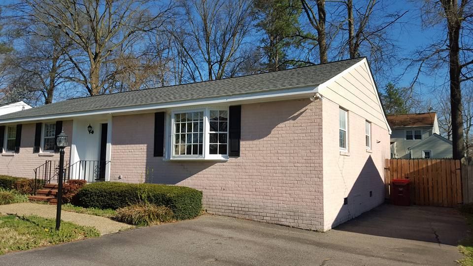 A pink brick house with black shutters and a driveway.