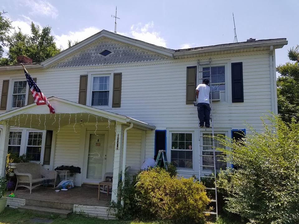 A man is painting the side of a white house.