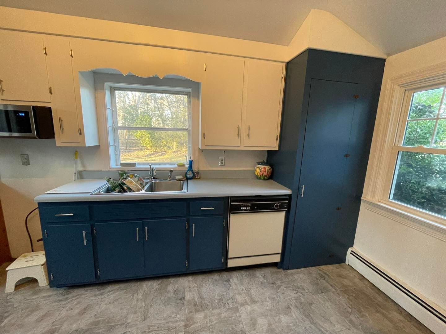 A kitchen with blue cabinets , a sink , a dishwasher , and a window.