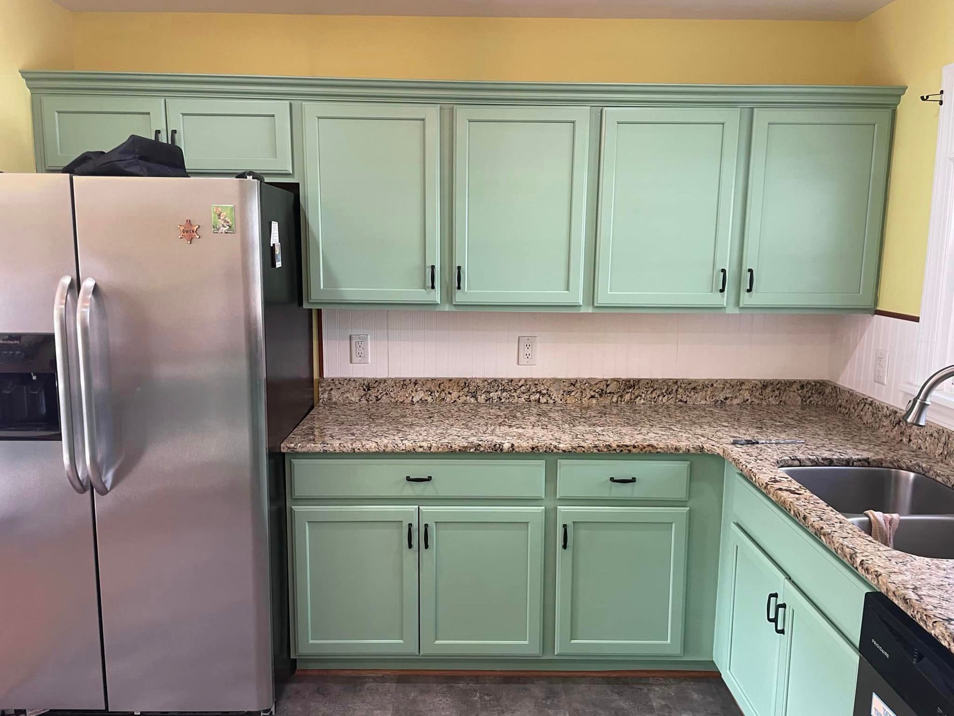 A kitchen with green cabinets and a stainless steel refrigerator
