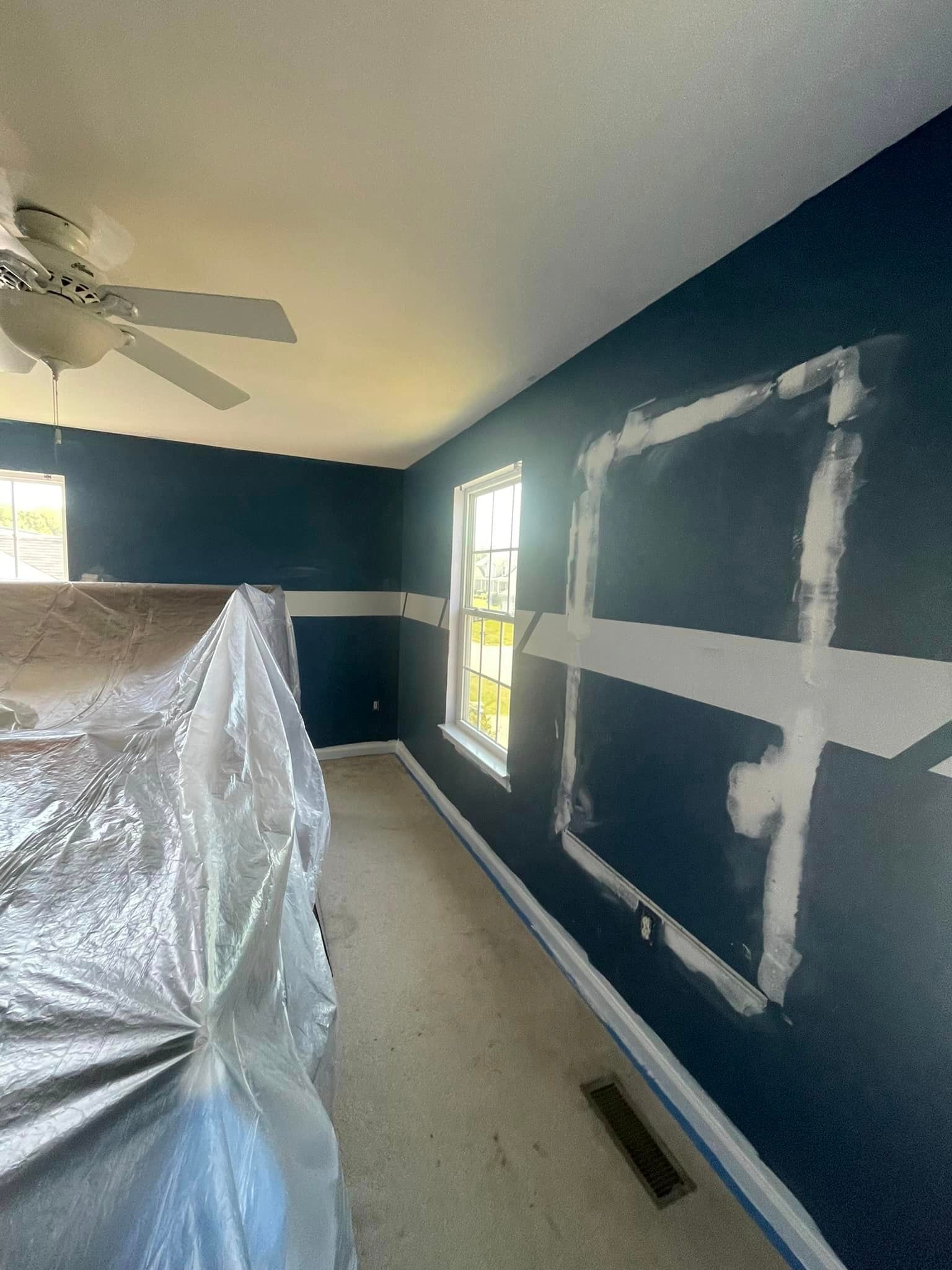 A room with blue walls and a ceiling fan is being painted.
