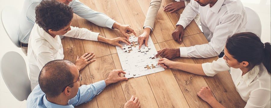 A group of people working together to solve a jigsaw puzzle on a wooden table.