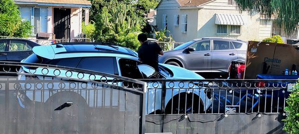 A man is standing next to a blue car parked in front of a house.