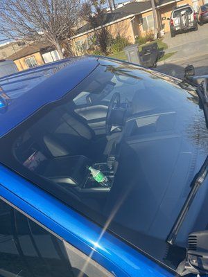 A blue car with a clear windshield is parked on the side of the road.