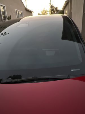 A close up of a red car 's windshield and hood