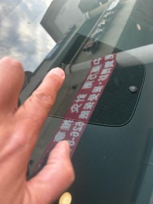 A person 's finger is pointing at a sticker on the windshield of a car