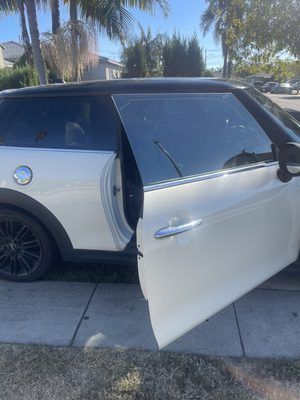 A white mini cooper is parked on the side of the road with its doors open.