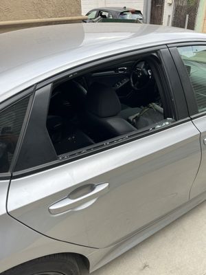 A silver car with a broken window is parked in a driveway.