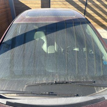 A car with a dirty windshield is parked in a driveway.