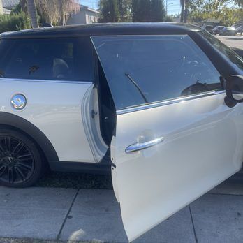 A white car with the door open is parked on the side of the road.
