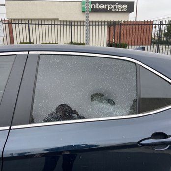 A car with a broken window is parked in front of an enterprise store