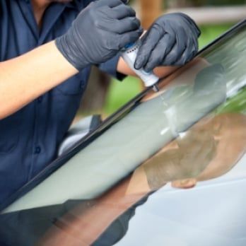 A man wearing gloves is working on a car windshield
