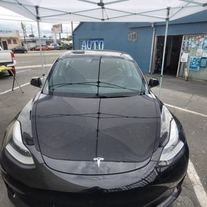 A black tesla model 3 is parked in a parking lot under a tent.