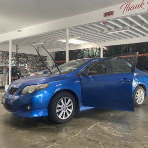 A blue car is parked in a garage with its doors open.