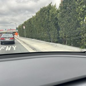 A car is driving down a highway next to a row of trees.