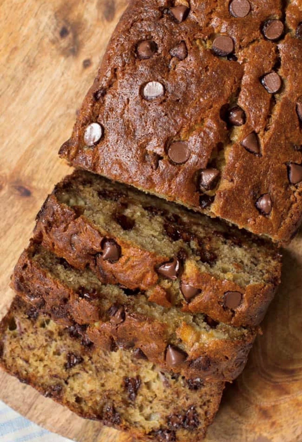 A loaf of banana bread with chocolate chips is sitting on a wooden cutting board.