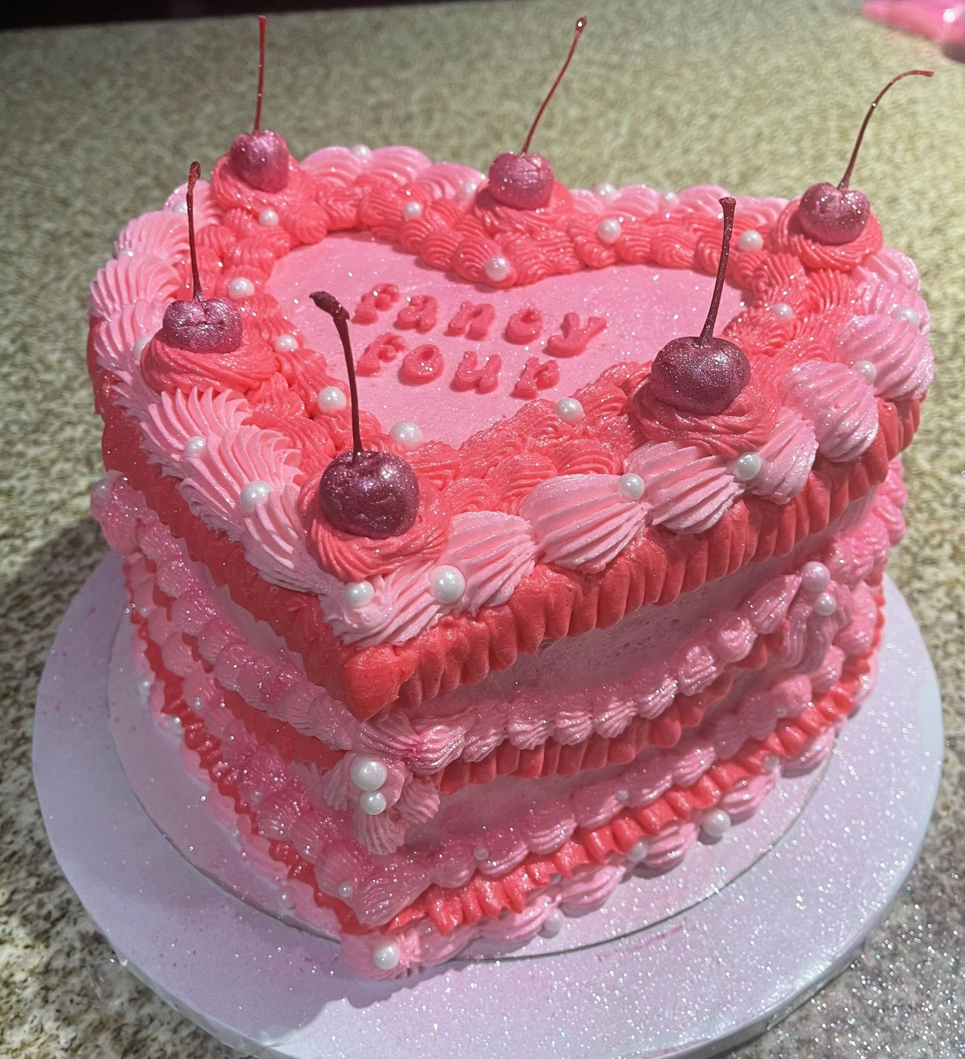 A heart shaped cake with pink frosting and cherries on top.
