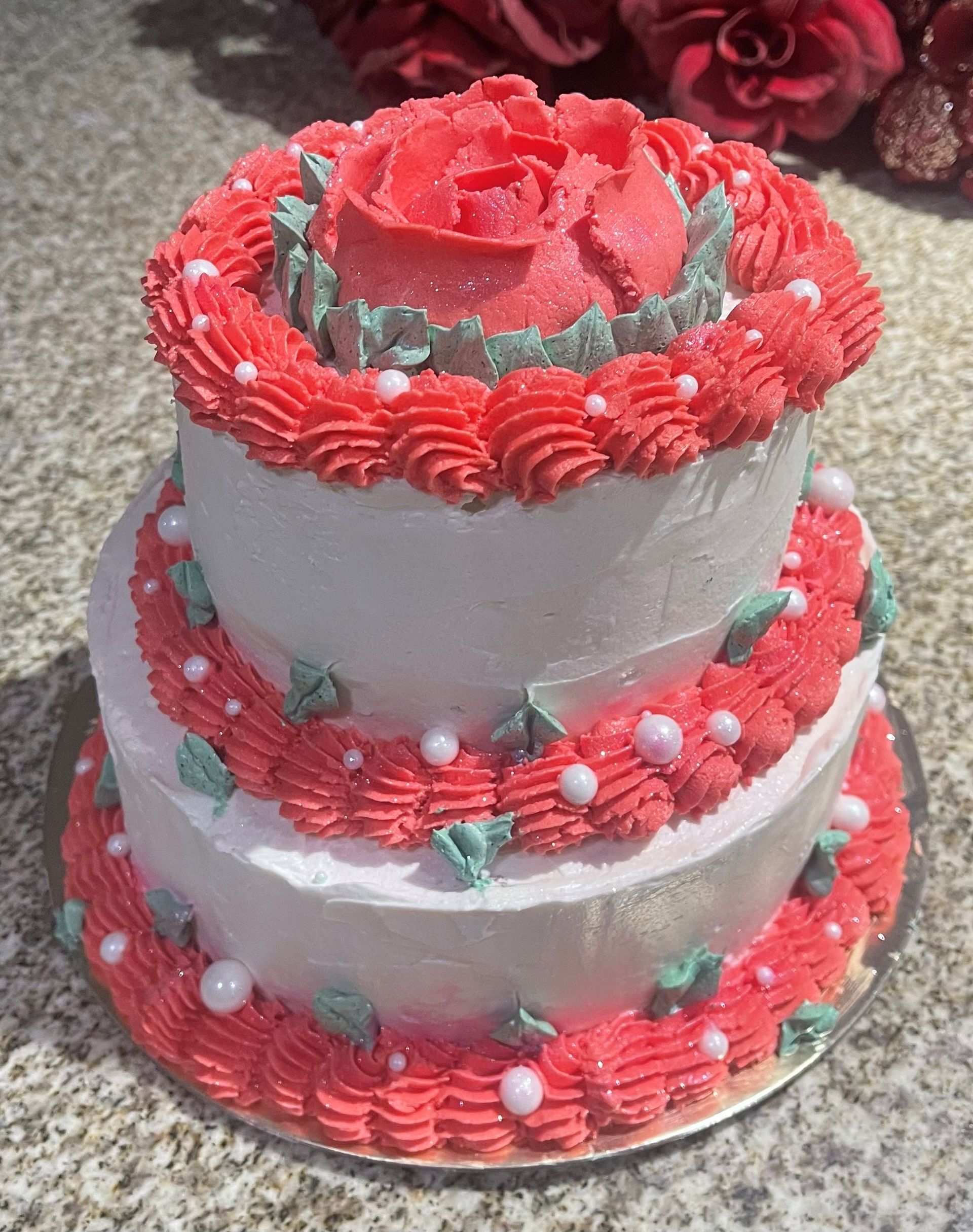 A two tiered cake with red frosting and a rose on top.