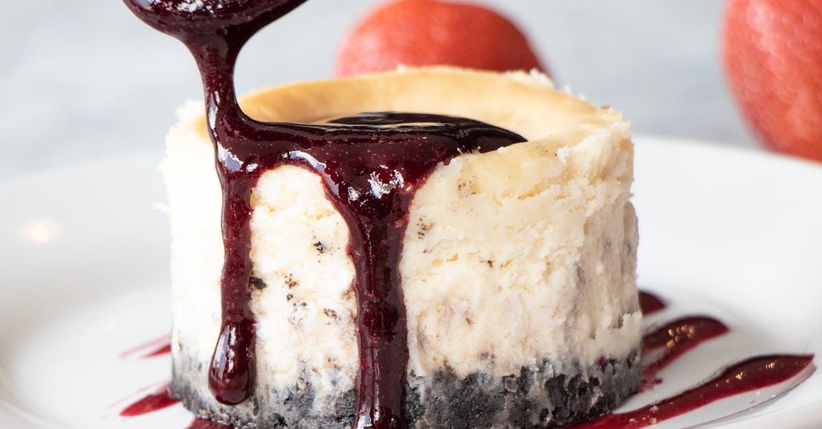 A close up of a cheesecake with sauce being poured on it on a plate.