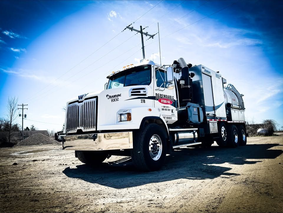 A white Western Star industrial vacuum truck parked on a dirt lot under a bright blue sky.