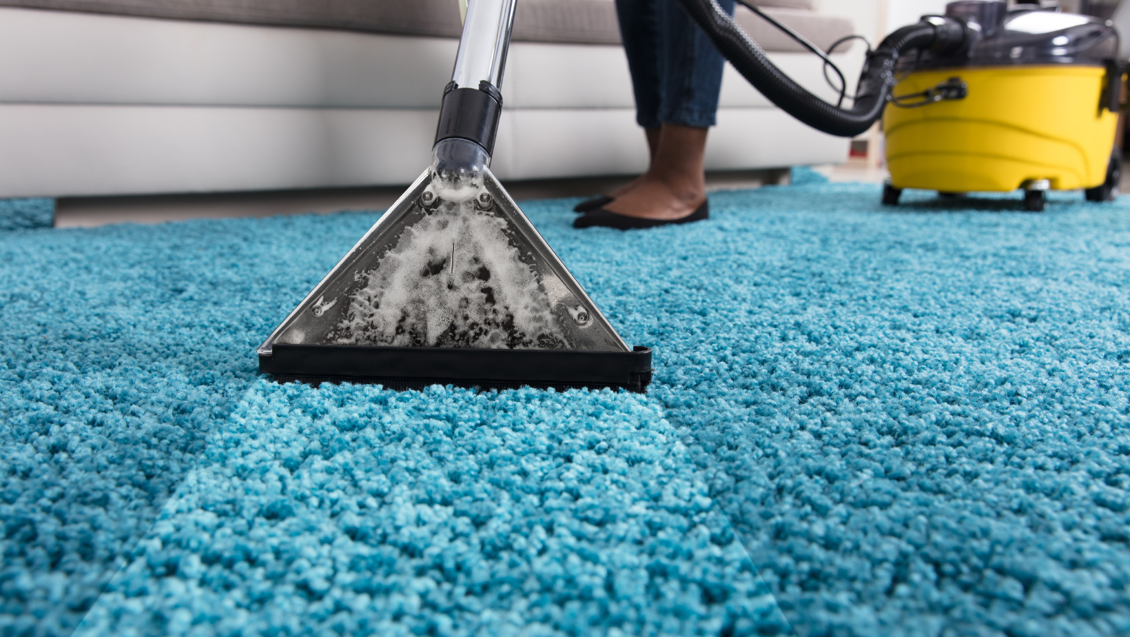 A person is cleaning a blue carpet with a vacuum cleaner.
