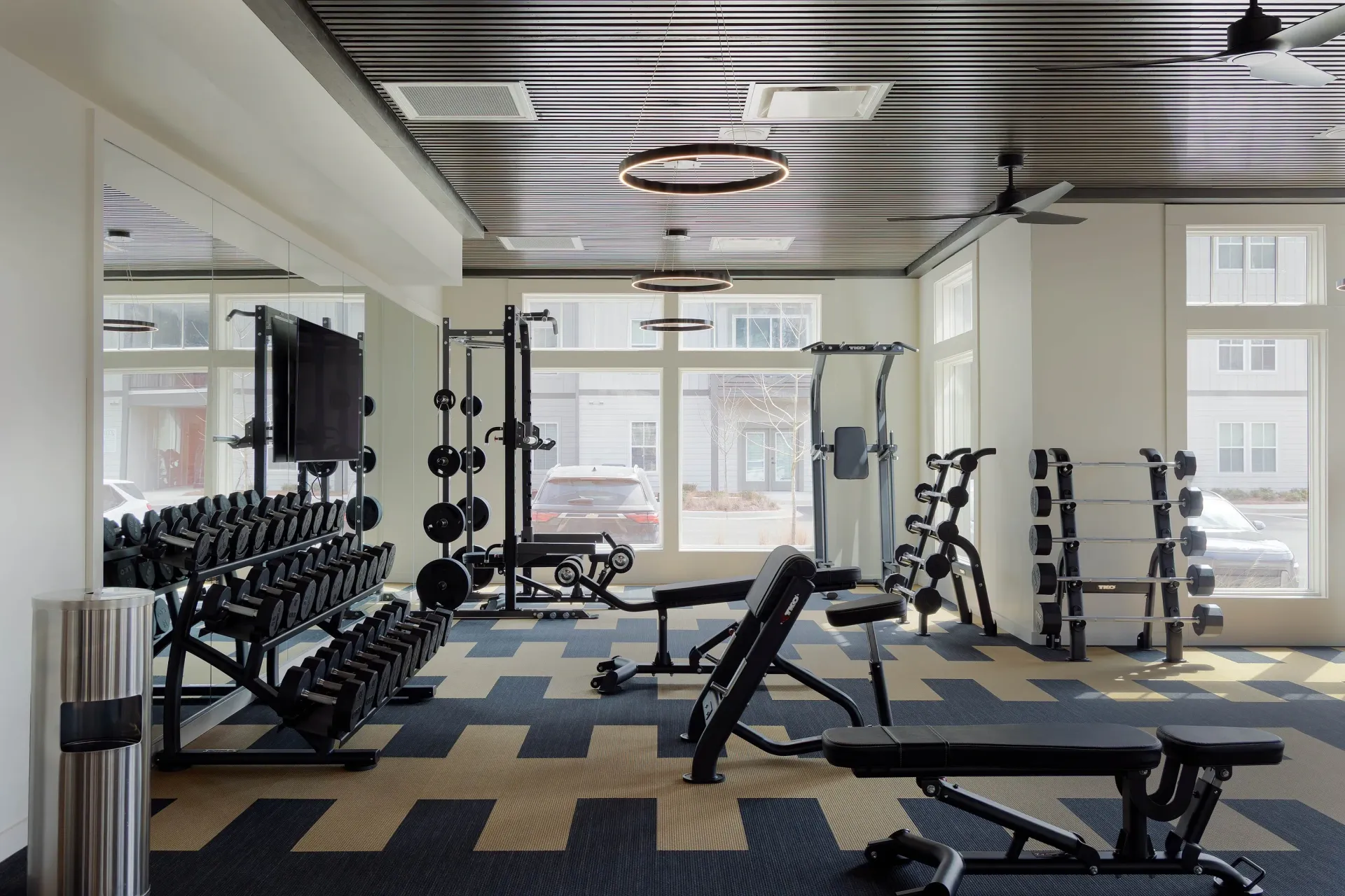Modern fitness center with dumbbells, weight racks, benches, and cardio equipment.