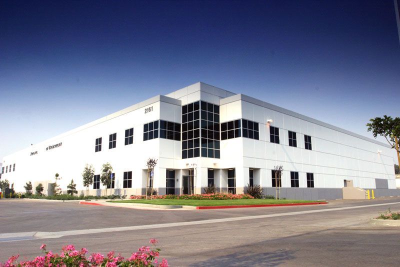 Building exterior with a grassy lawn and trees. Beige and black facade, sunny day.