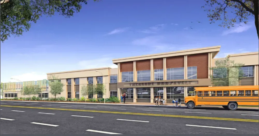 Commercial building with tan and white facade, windows, and parking spaces. Blue sky and greenery.