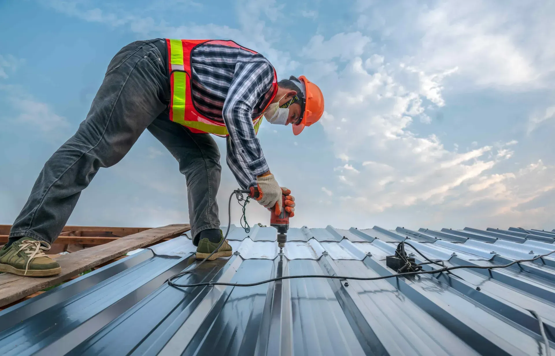 Roofer in safety gear, kneeling on a rooftop, hammering shingles.