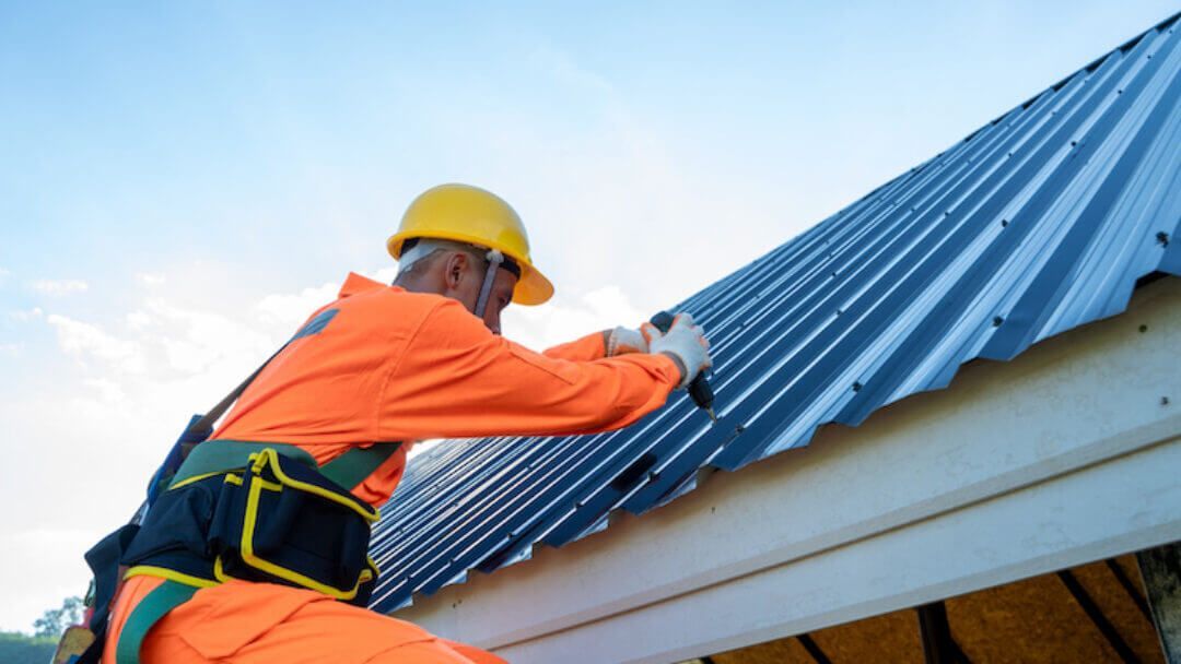 Construction workers installing roofing materials on a rooftop, wearing safety vests and hard hats.