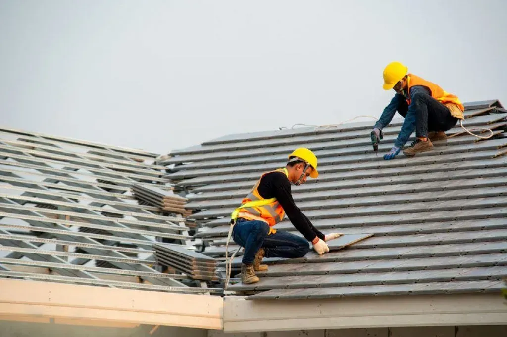 Construction worker with chainsaw and hammer, standing on a rooftop, city skyline in background.