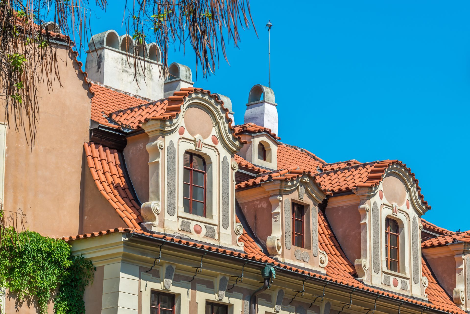 Roofer on a dark tiled roof, holding bundles of roofing materials. Wearing a cap and tool belt.