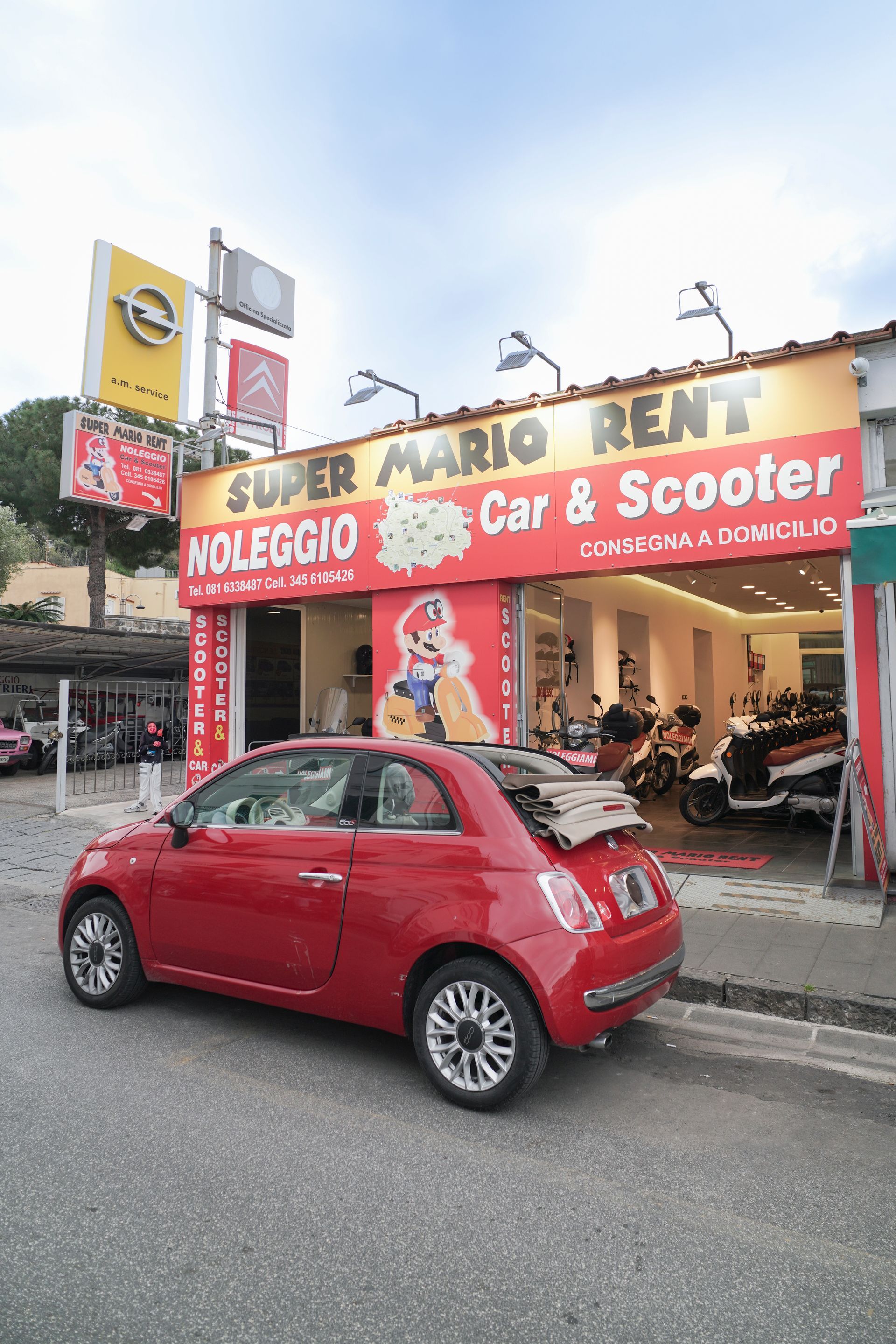 Un'auto rossa è parcheggiata davanti a un negozio di noleggio auto e scooter di Super Mario.