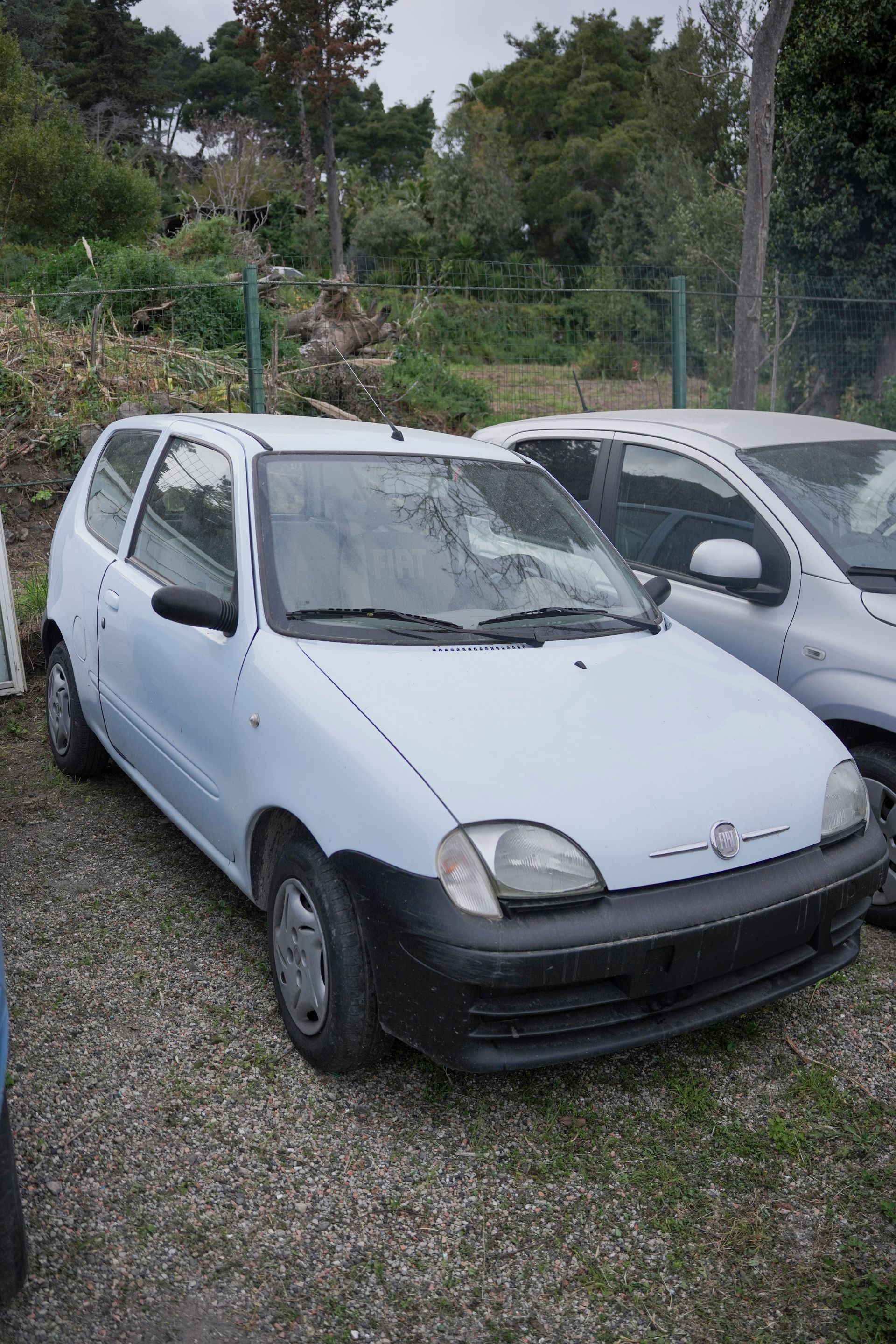 Un'auto bianca è parcheggiata accanto a un'altra auto in un parcheggio ghiaioso.