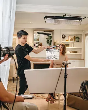 A man is holding a clapper board in front of a woman in a living room.