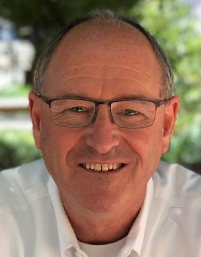 A man wearing glasses and a white shirt is smiling for the camera.