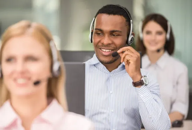 A man wearing a headset is talking on a phone in a call center.