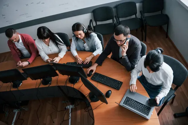 A group of people are sitting around a table working on computers.