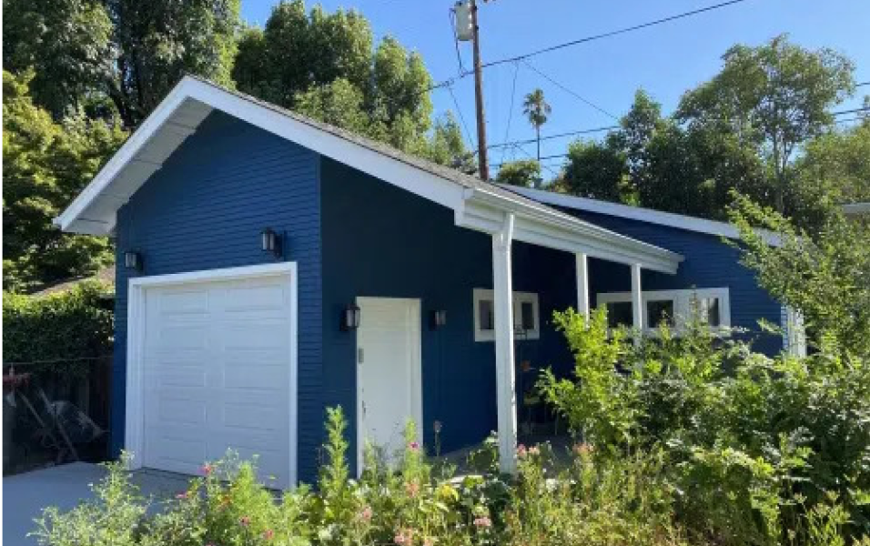 A blue house with a white garage door is surrounded by trees.