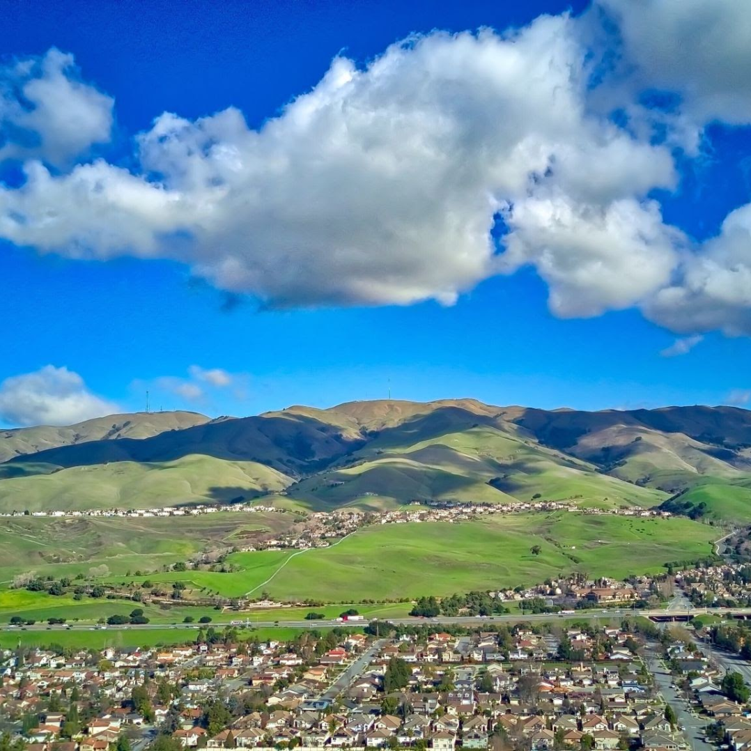 An aerial view of a city with mountains in the background and clouds in the sky.