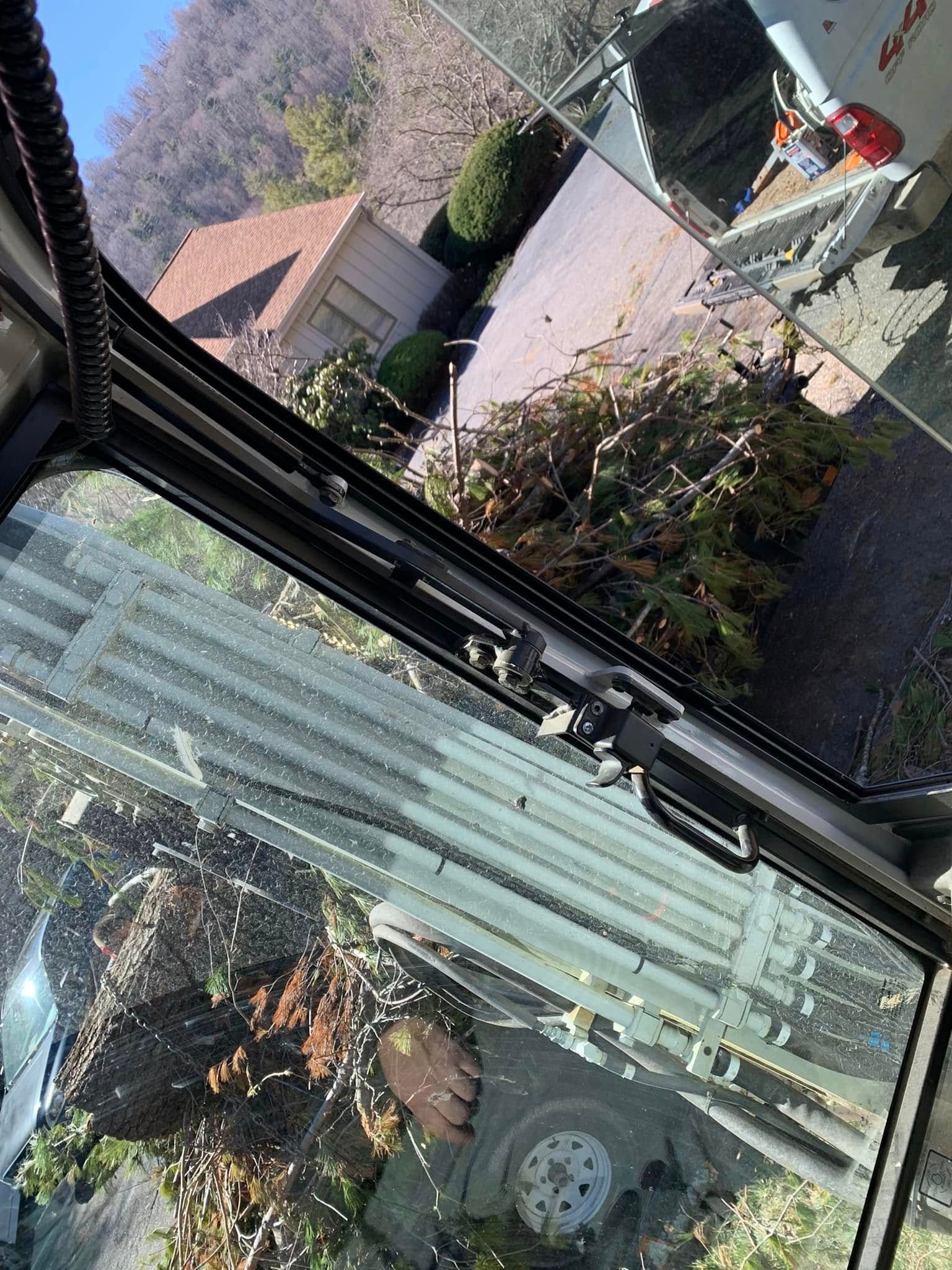 View from inside a vehicle looking through a window at a suburban house with a brown roof and surrounding greenery.