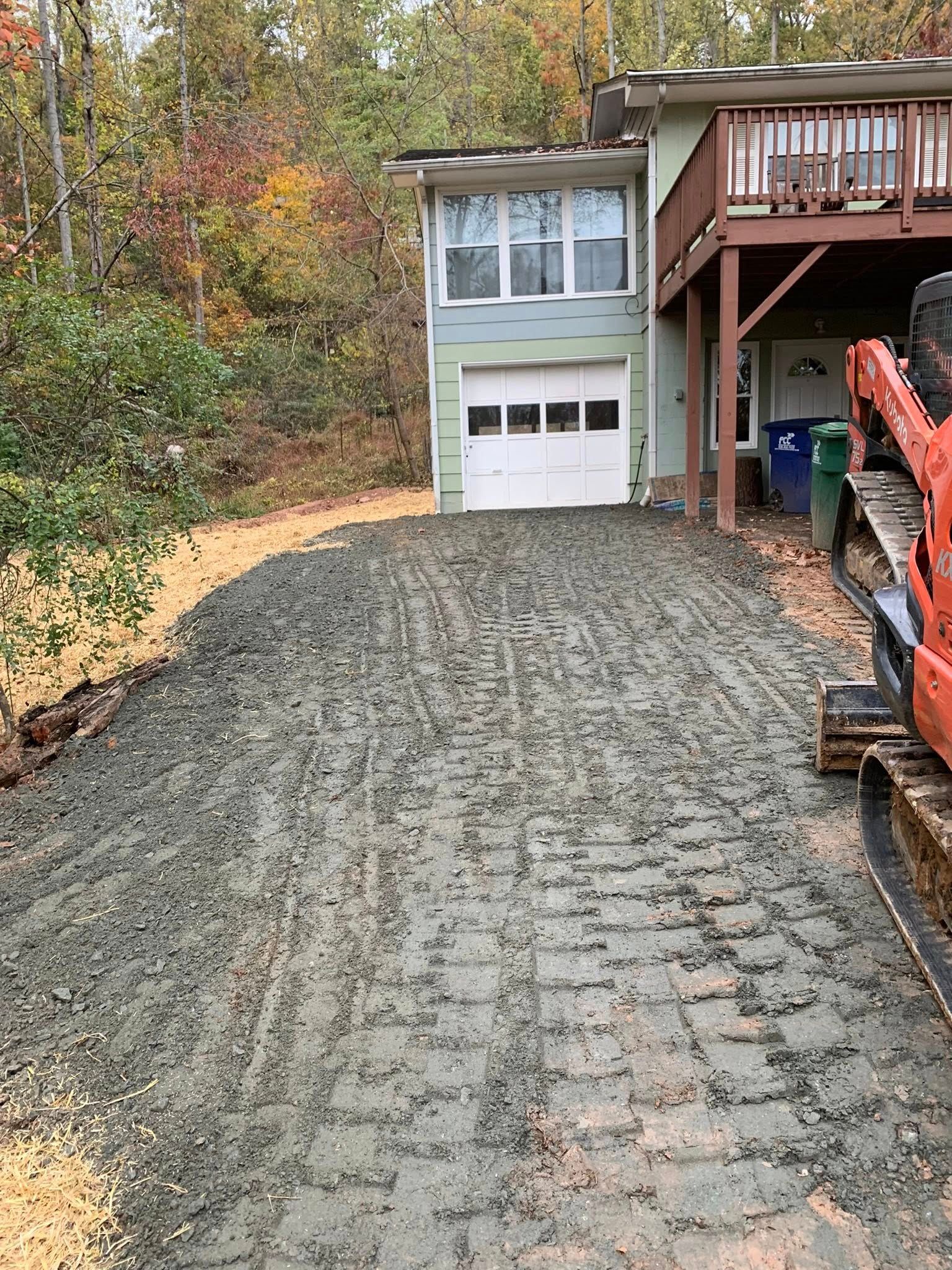 A gravel driveway leads to a light green house with a white garage door and an elevated wooden deck.