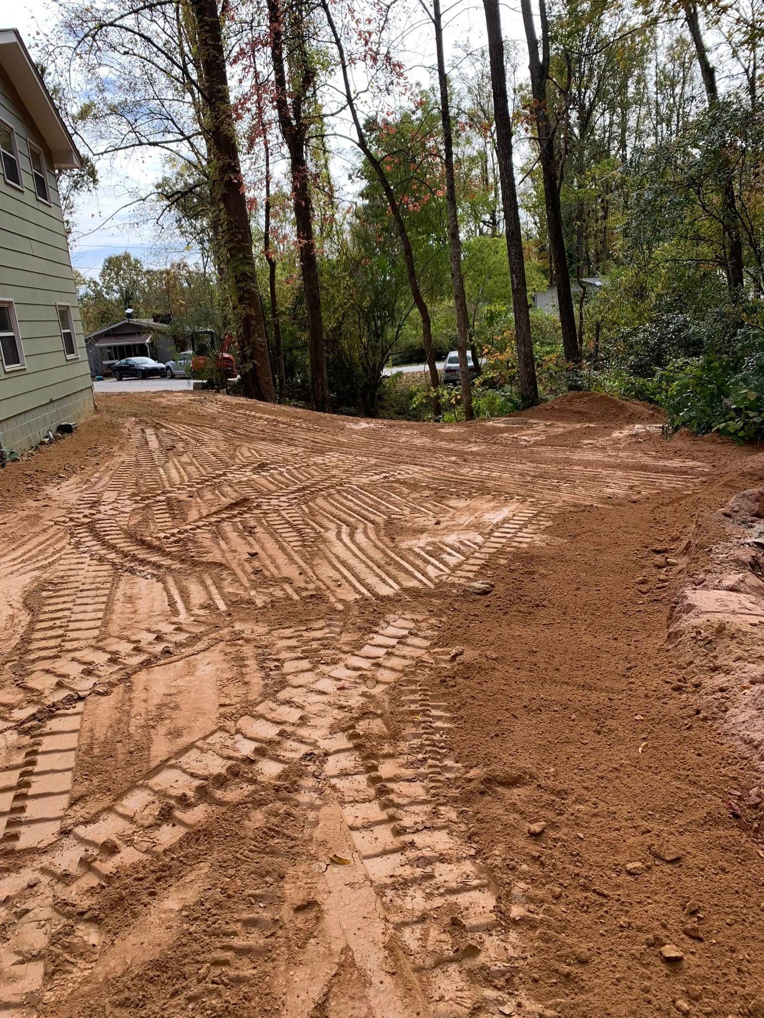 A backyard area features exposed, freshly turned brown soil marked by deep tire tracks from construction equipment.