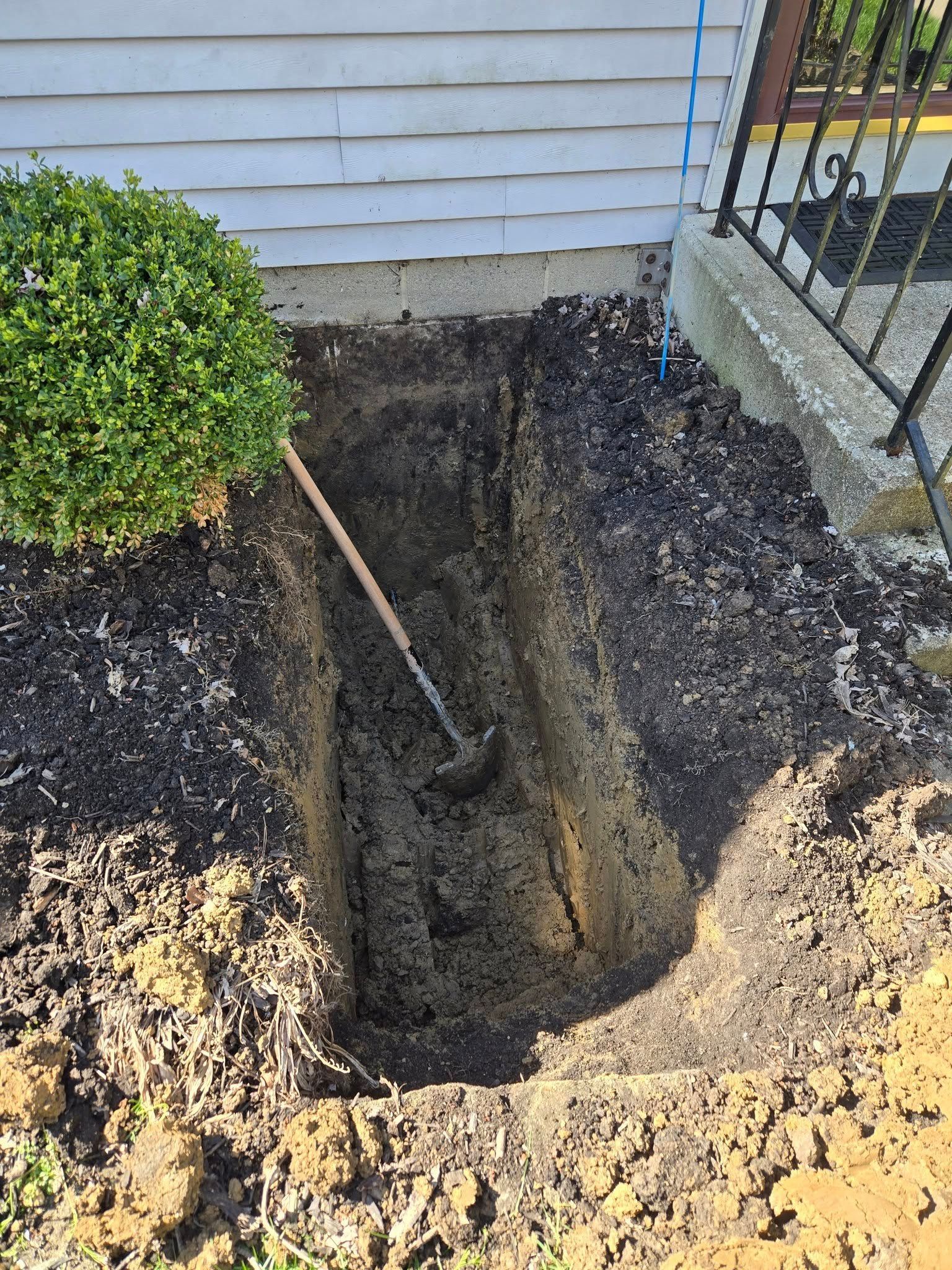A hole in the ground next to a house with a shovel in it.