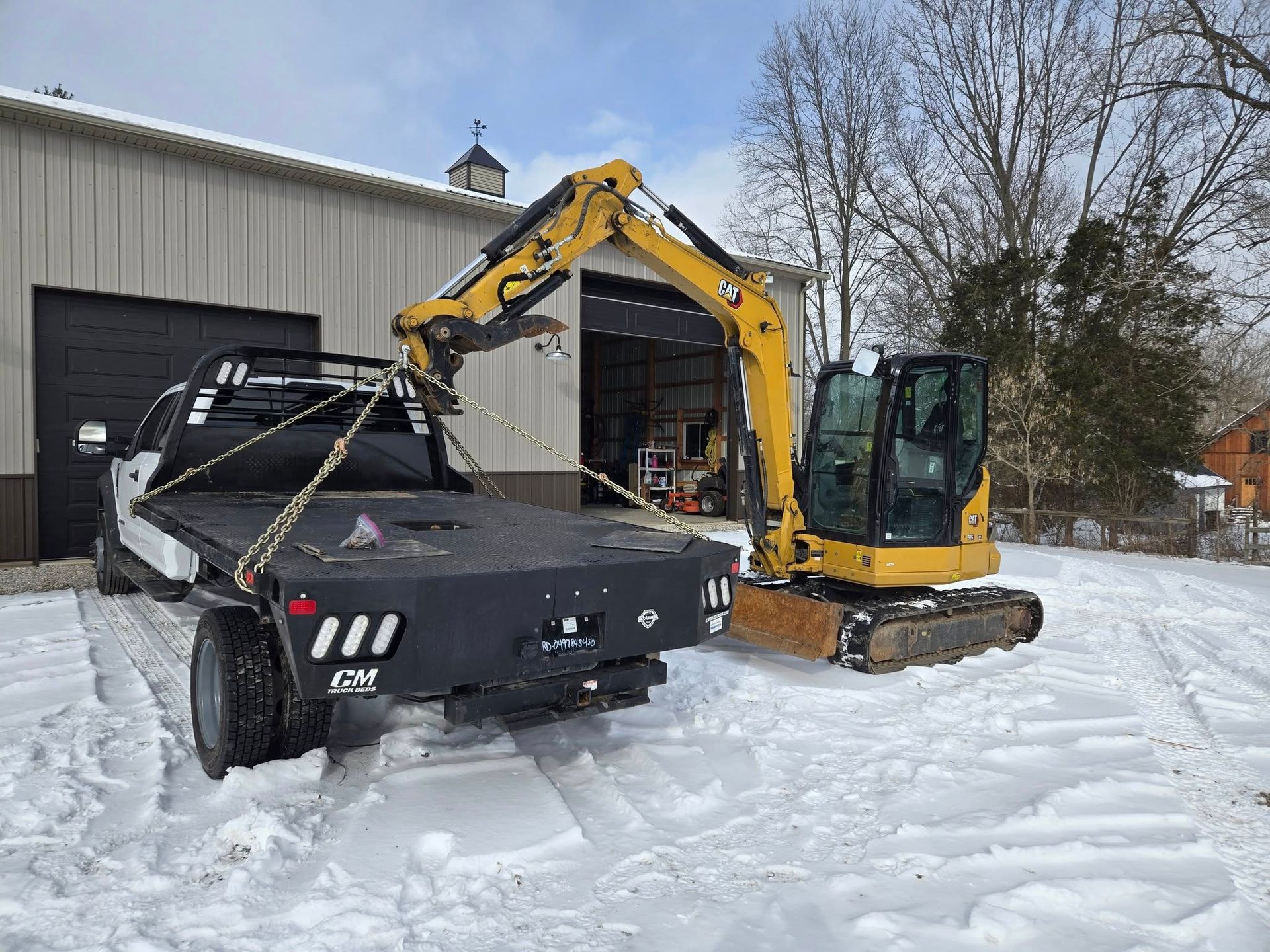 A truck is being towed by an excavator in the snow.