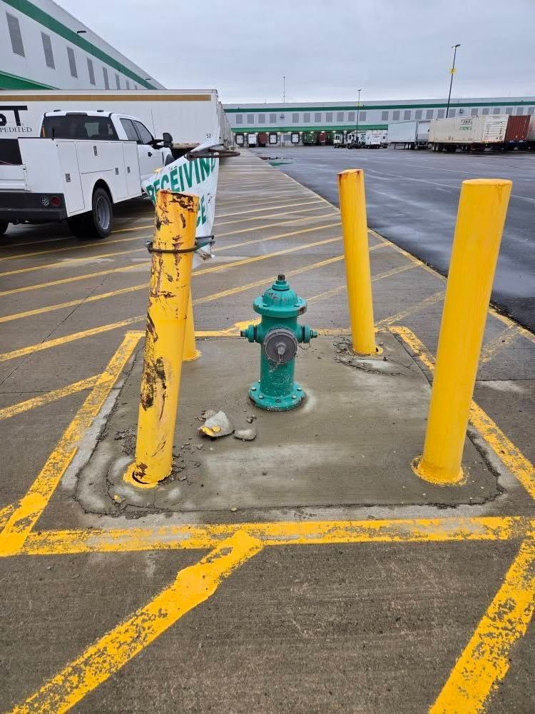 A green fire hydrant is sitting in a parking lot next to yellow poles.