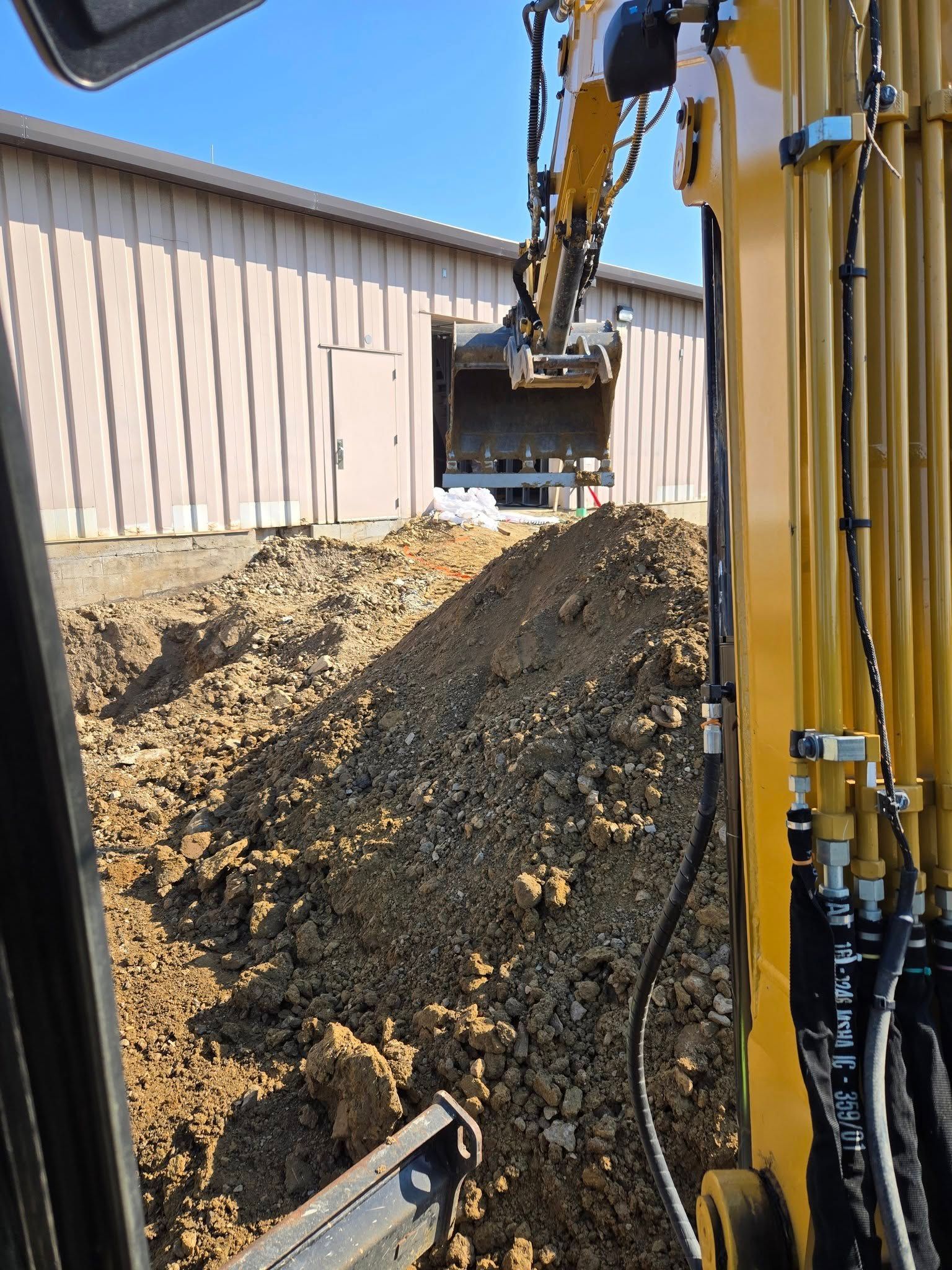 A yellow excavator is moving dirt in front of a building.