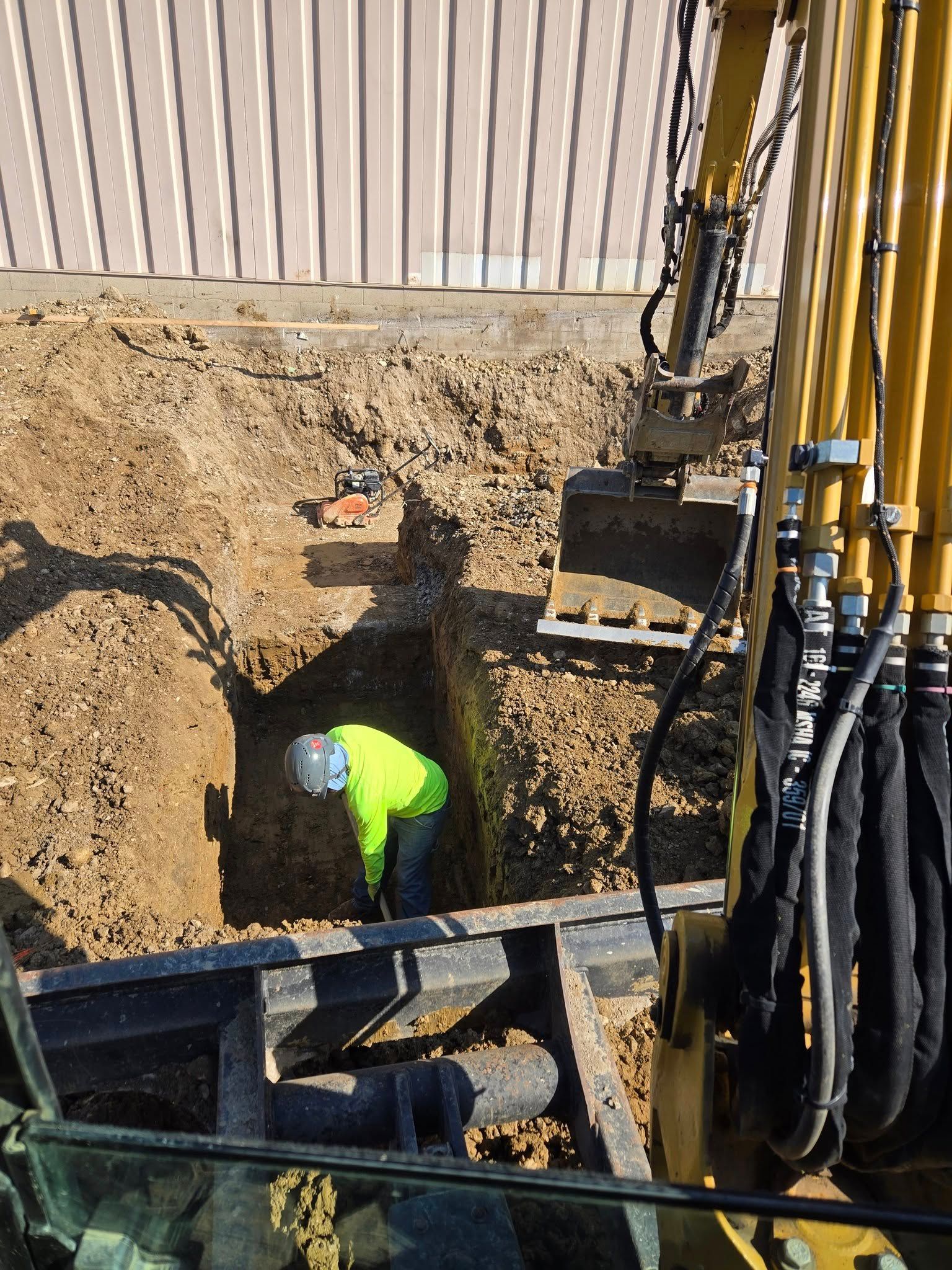 A man is digging a hole in the ground next to a yellow excavator.