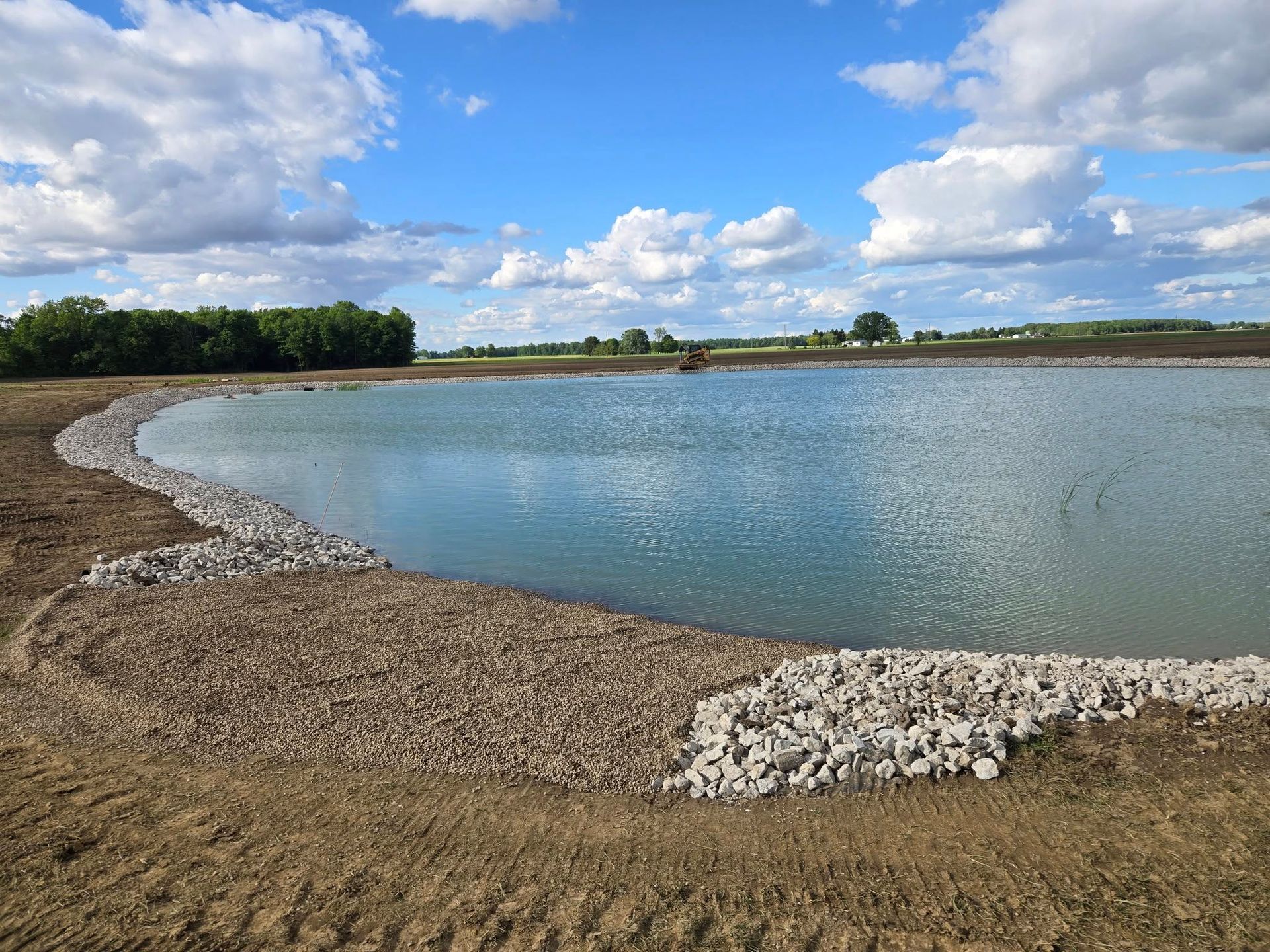 A large body of water is surrounded by gravel and trees